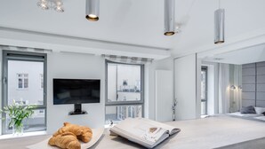 A modern living room with a flat-screen TV, a large window, and a breakfast setup with croissants. - Elite Apartments Old Town Prestige (Gdansk)