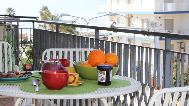 A balcony with a table set for breakfast, including oranges, a bowl, and a mug. - Lucy Apartment (Ragusa)