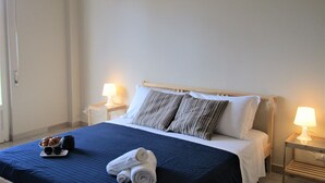 A neatly made bed with a blue bedspread, two pillows, and a bedside table with a lamp. - Lucy Apartment (Ragusa)