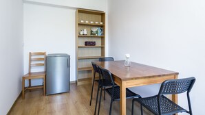 Habitación pequeña con una mesa de comedor de madera, sillas negras, un refrigerador compacto y una estantería con diversos objetos.