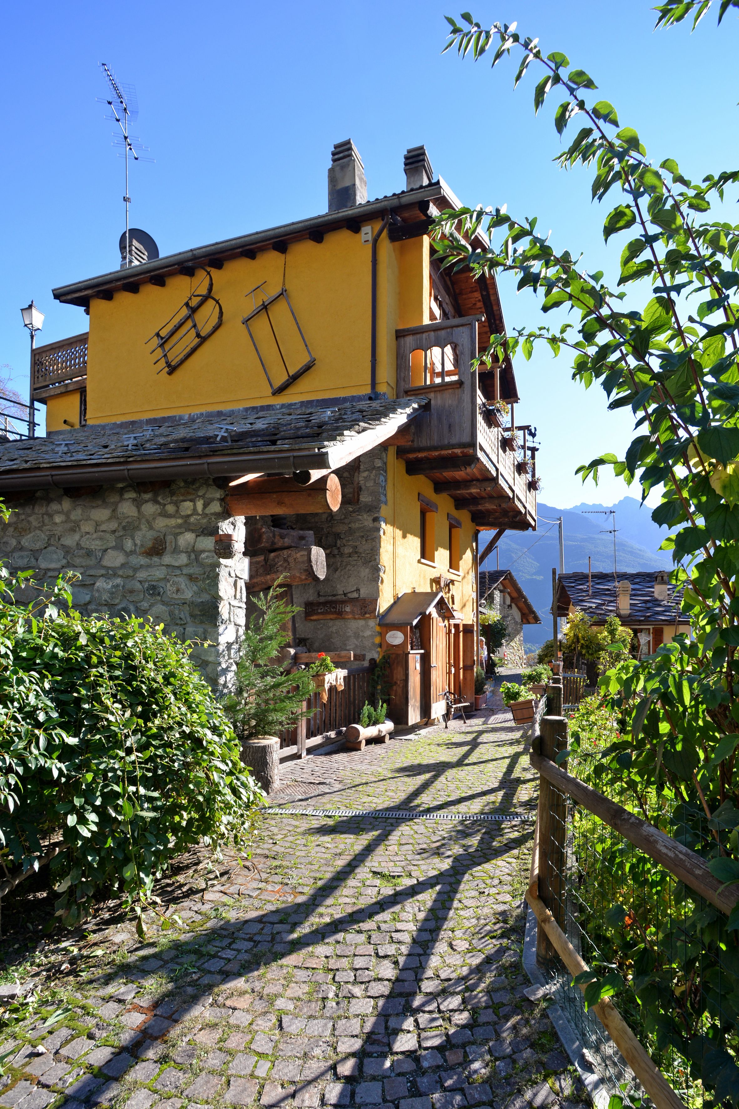Una strada acciottolata che conduce a un edificio giallo con un balcone in legno.
