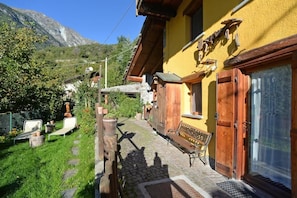 Un bâtiment jaune avec un porche en bois, un banc et une porte dotée d’une fenêtre.