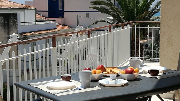 A balcony with a table set for breakfast, including fruits, bread, and cups. - Mary Holidays House (Ragusa)