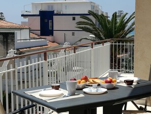 Un balcon avec une table préparée pour le petit-déjeuner, comprenant des fruits, du pain et des tasses.