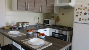 A modern kitchen with wooden cabinets, a gas stove, a microwave, and a refrigerator. - Mary Holidays House (Ragusa)