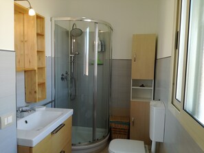 A bathroom with a glass-enclosed shower, a sink, a toilet, and wooden cabinets.