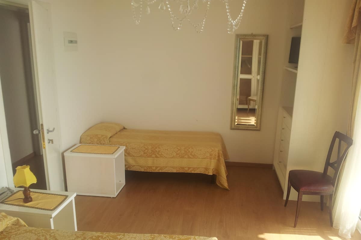 A small, well-lit room with a bed, a chair, a desk, and a wardrobe.