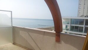 Un balcon avec vue sur la mer, un sol carrelé et une vue partielle sur un immeuble.