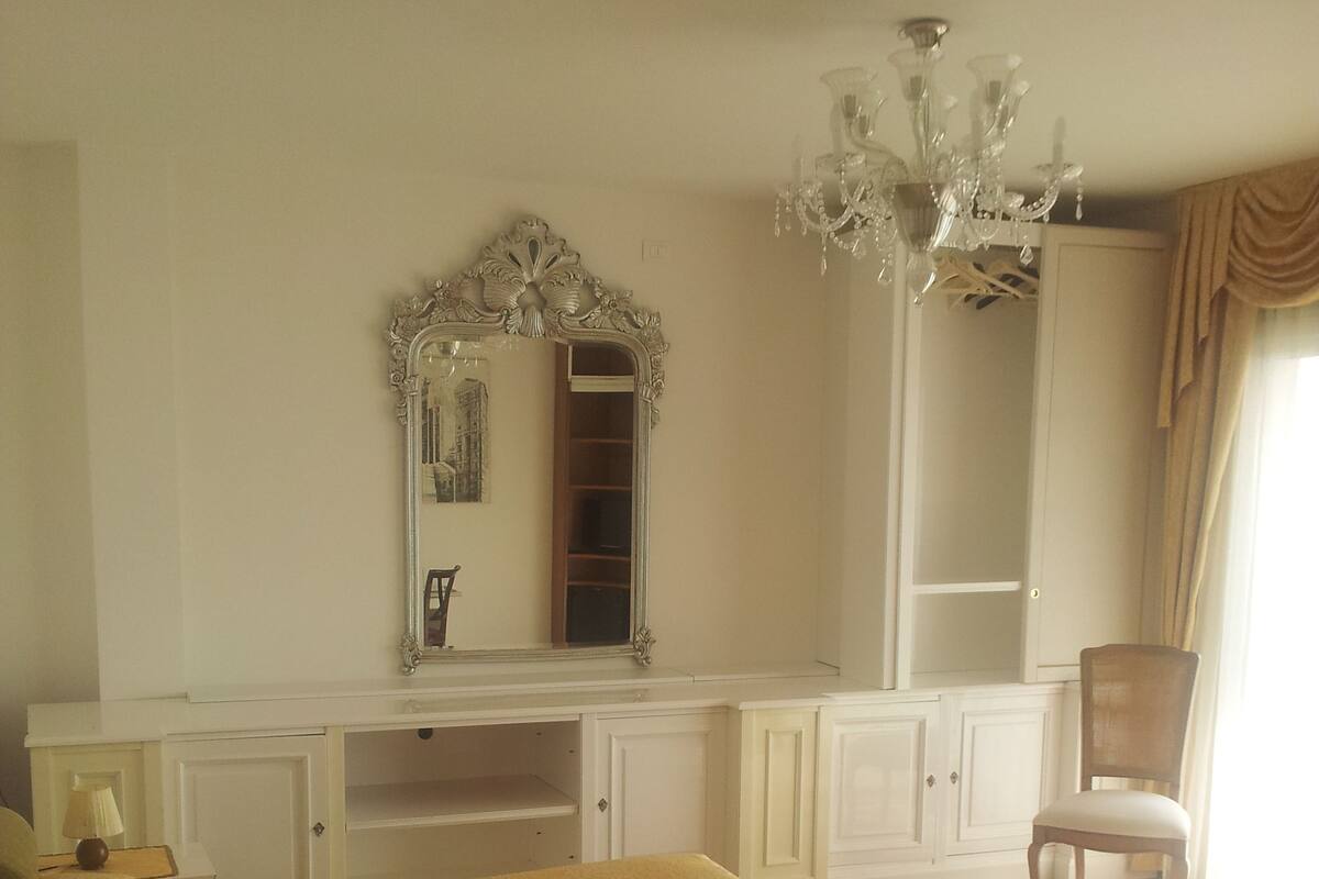 A bedroom with a large bed, a vanity with a mirror, a chandelier, and a chair.