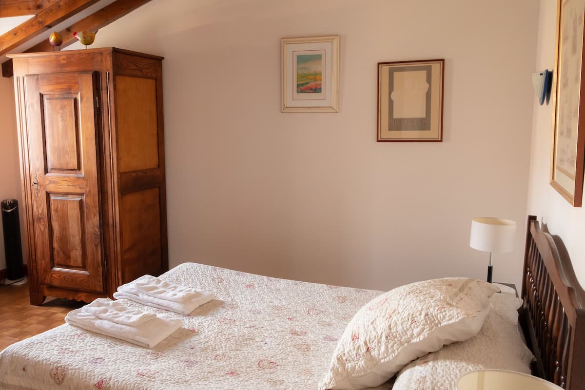 A bedroom with a wooden wardrobe, a bed with a quilt, and two framed pictures on the wall.