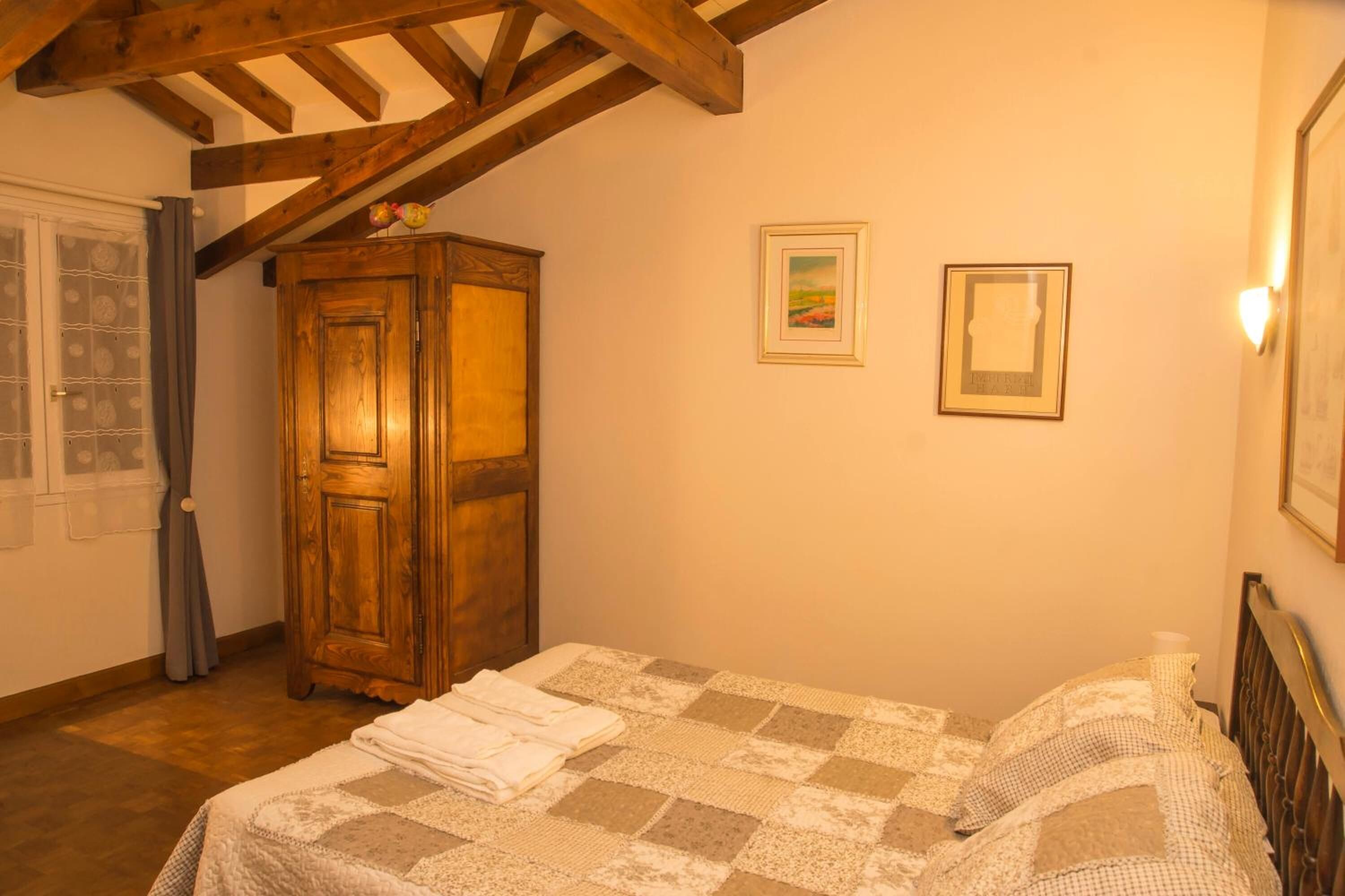Un dormitorio con un armario de madera, una cama con colcha a cuadros y dos cuadros enmarcados en la pared.