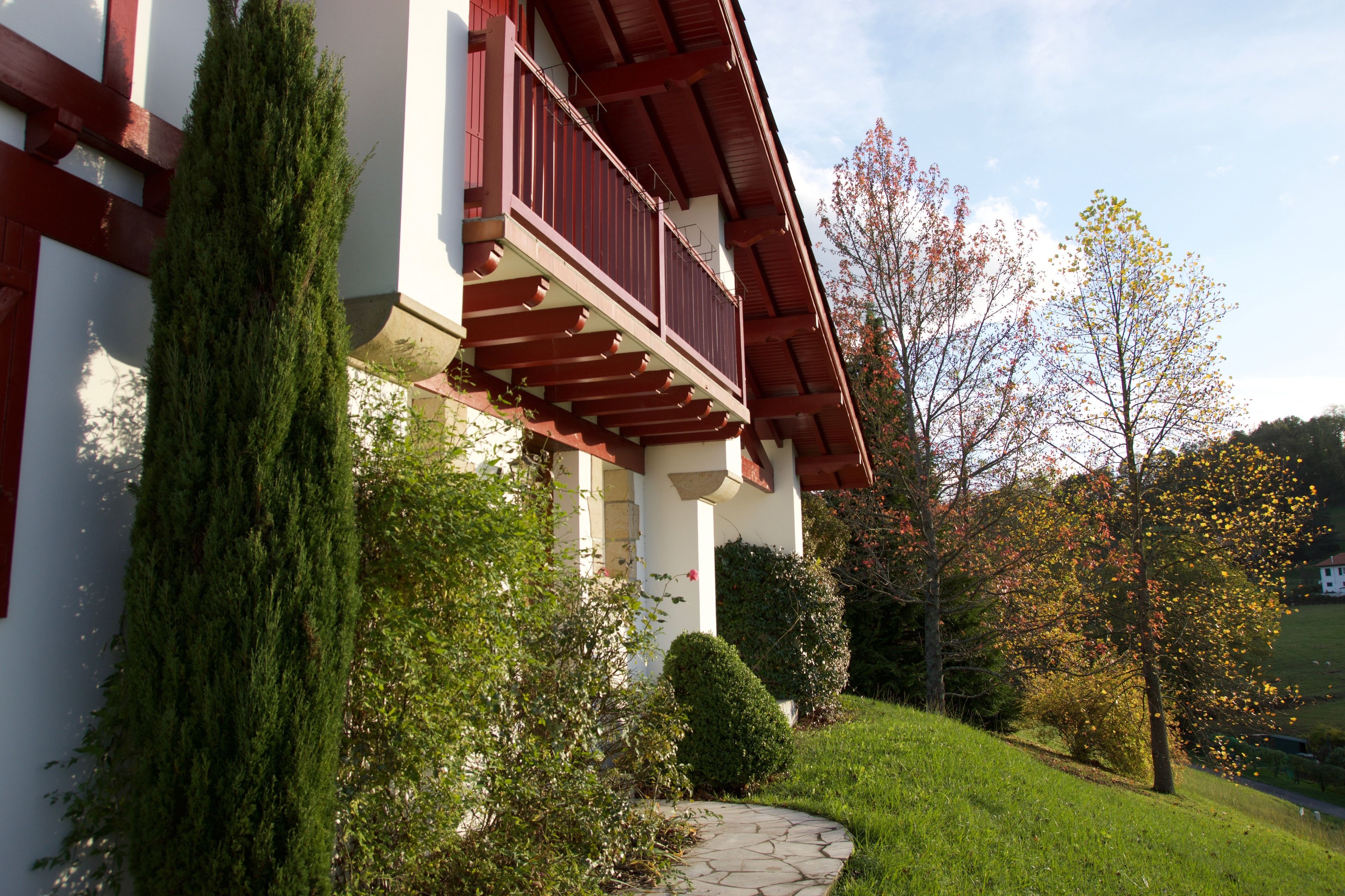 A building with a red balcony, a stone pathway, and surrounding greenery.