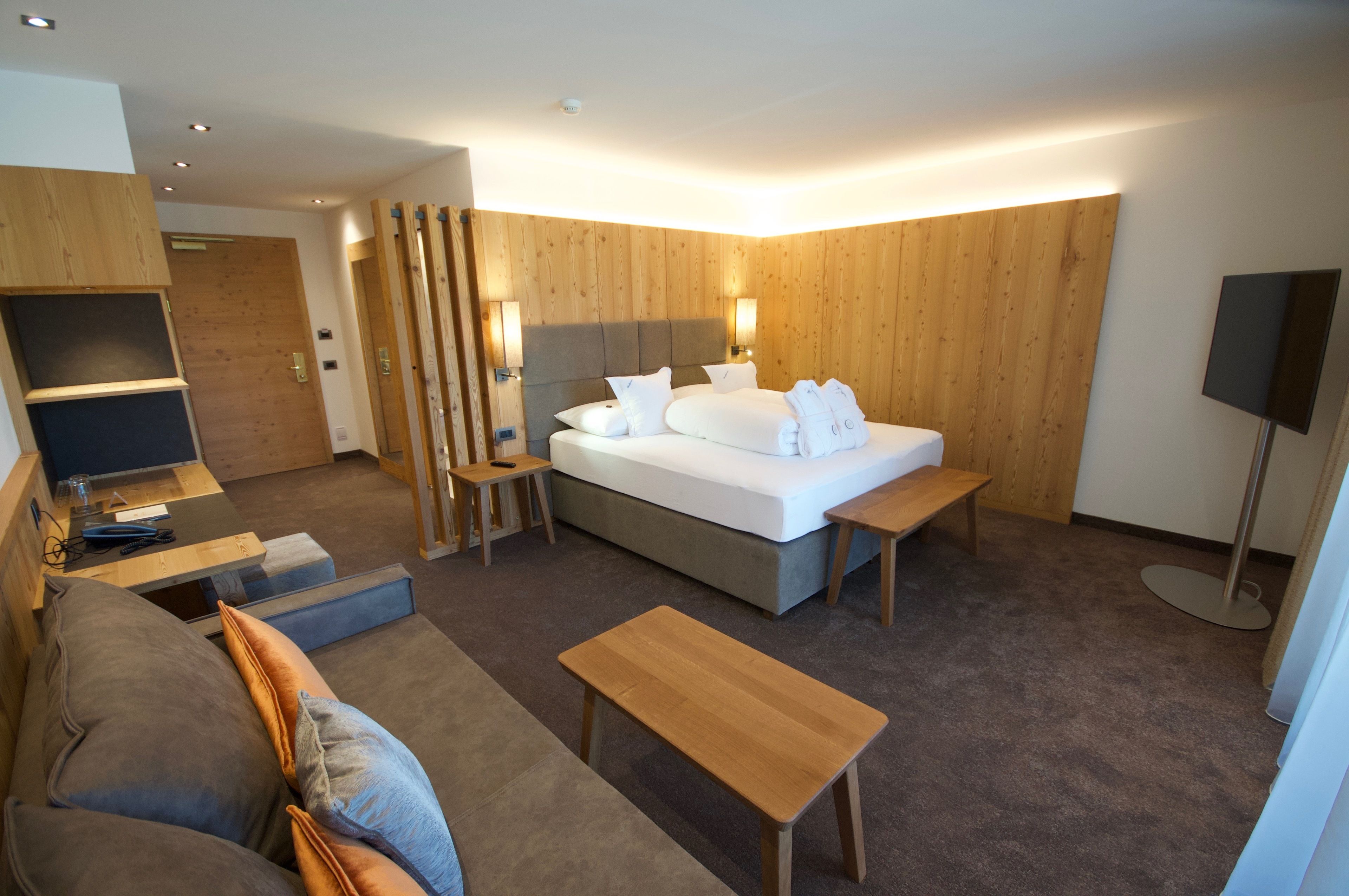 Una habitación de hotel moderna con cama, sofá, una mesita y televisión.