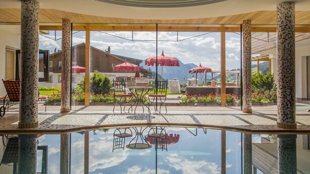 Ein überdachter Außenbereich mit Pool, roten Sonnenschirmen und Gartenmöbeln.