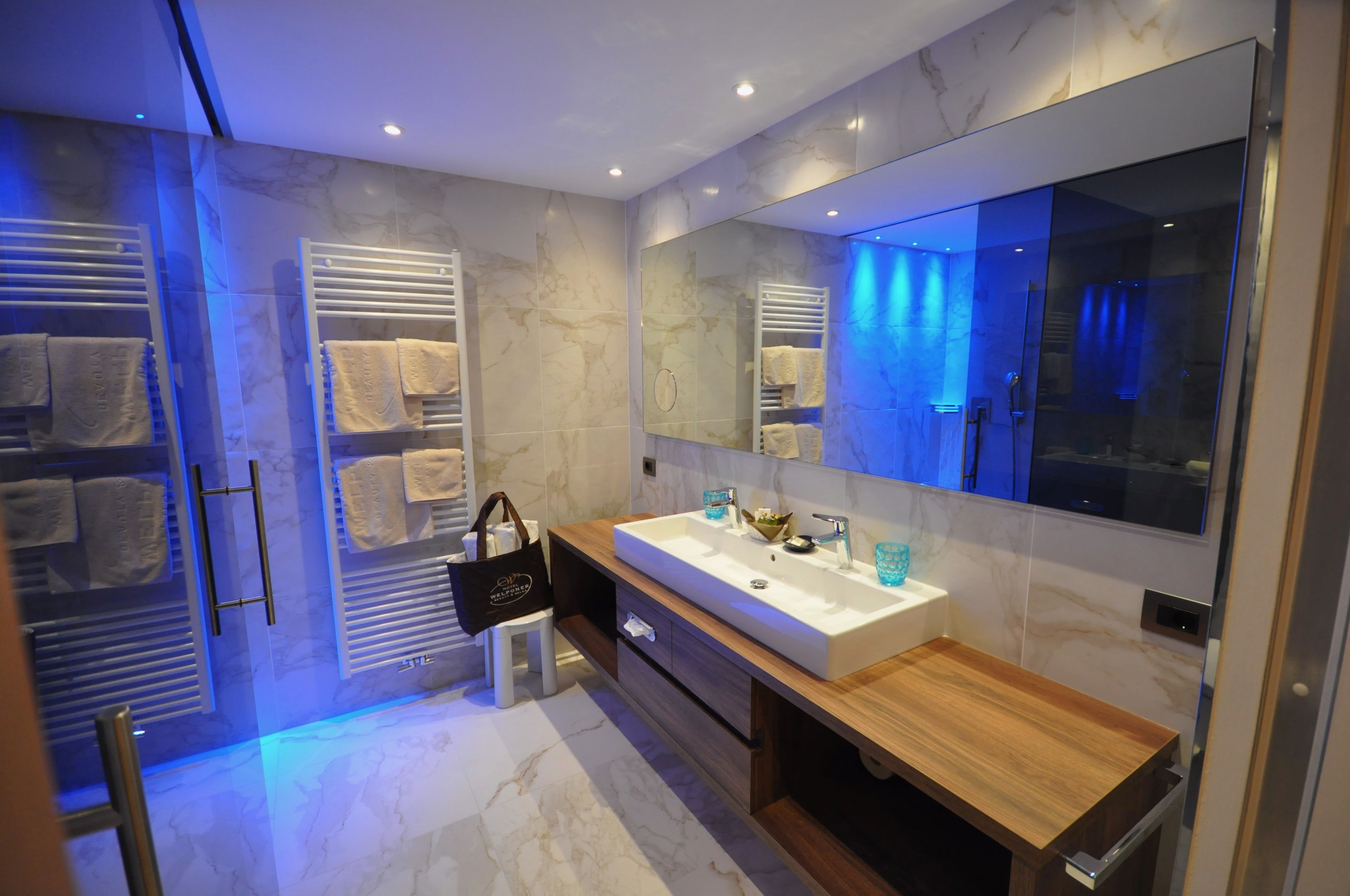 A modern bathroom with a large mirror, a wooden vanity, and towel racks.