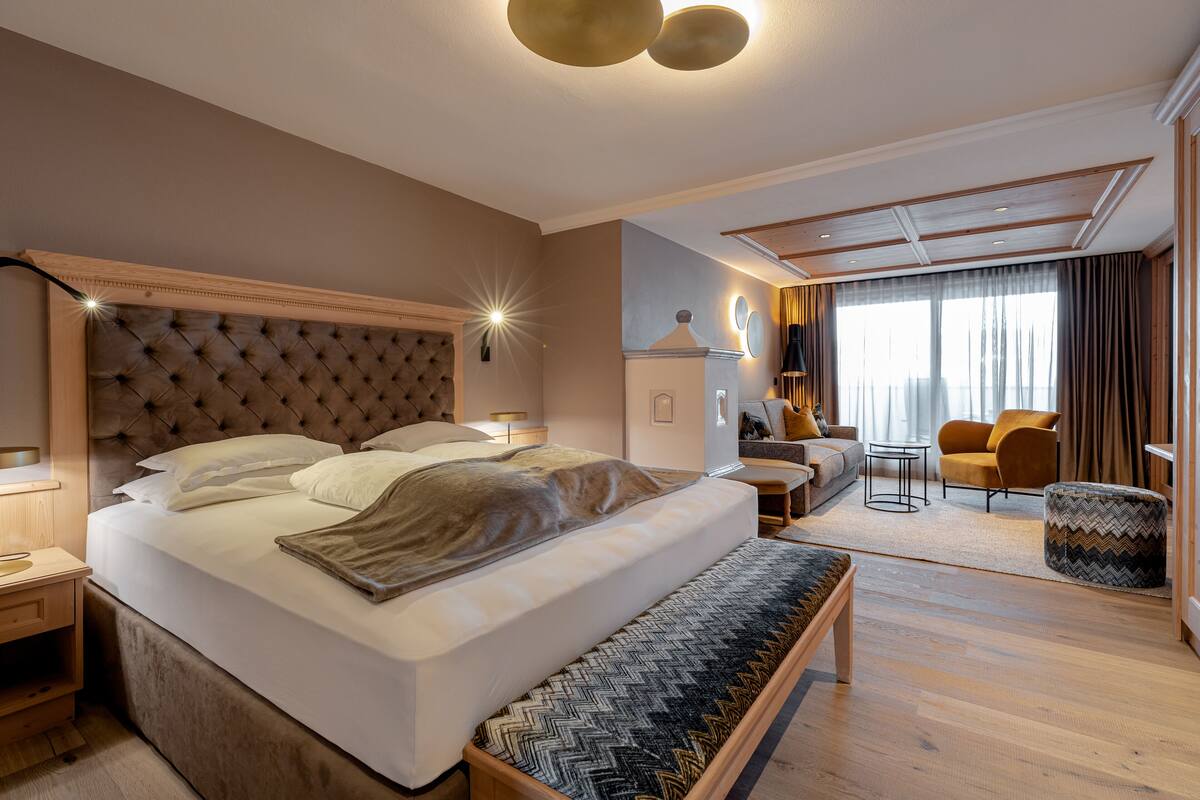 A modern hotel room with a large bed, a bench, a desk, and a sofa.