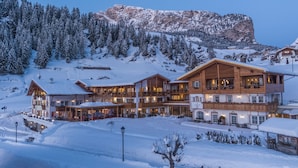 Ein großes, mehrstöckiges Chalet mit Holzfassade und mehreren Balkonen, umgeben von schneebedeckten Bergen und Bäumen.