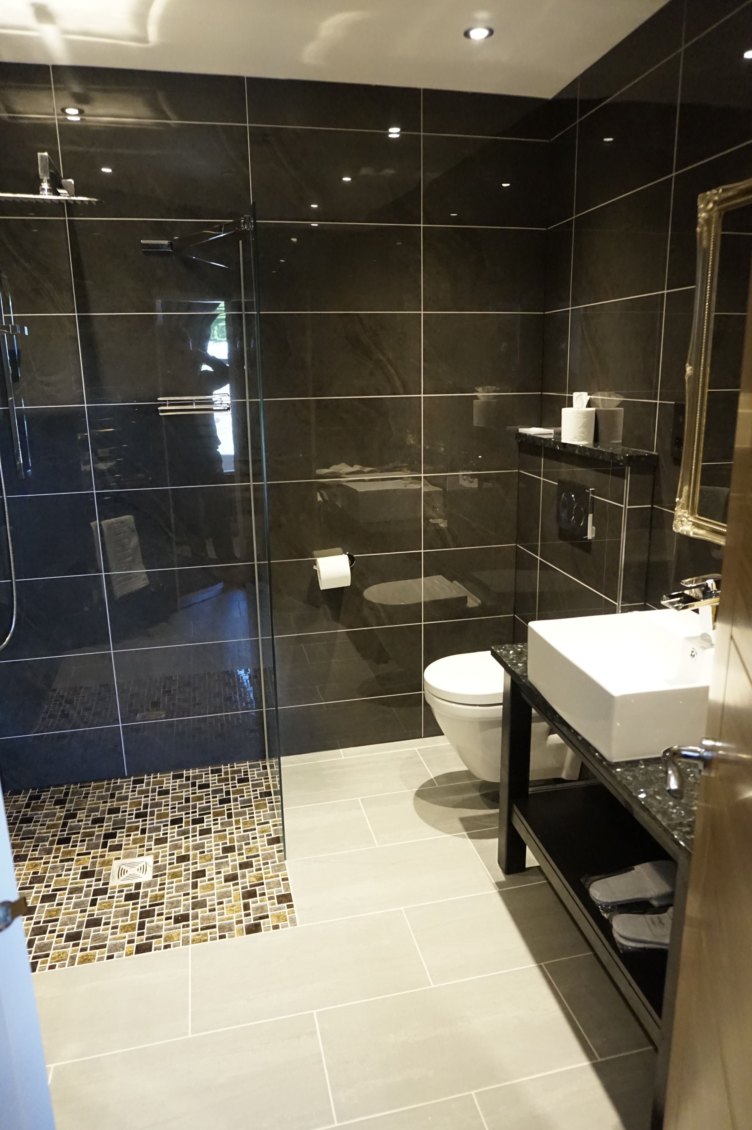 Un baño moderno con ducha envuelta en vidrio, inodoro blanco y tocador negro con espejo.