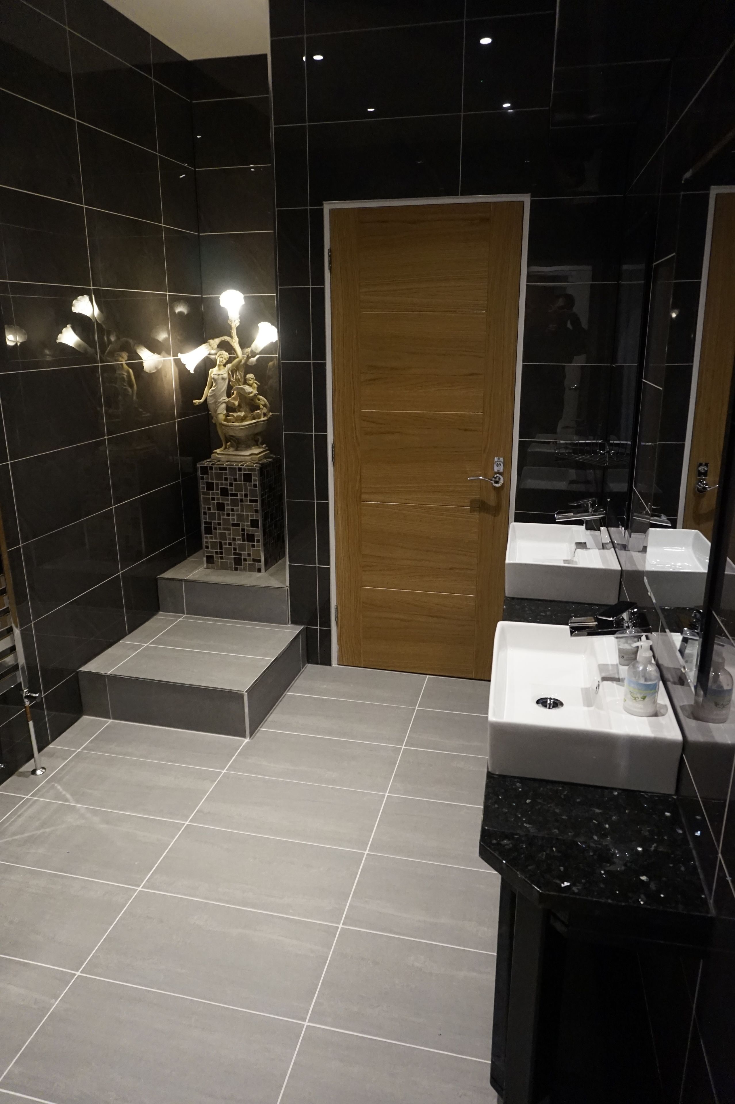 A modern bathroom with black tiles, a wooden door, and a white sink with a mirror.