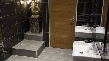 A modern bathroom with black tiles, a wooden door, and a white sink with a mirror.