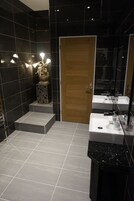 A modern bathroom with black tiles, a wooden door, and a white sink with a mirror.