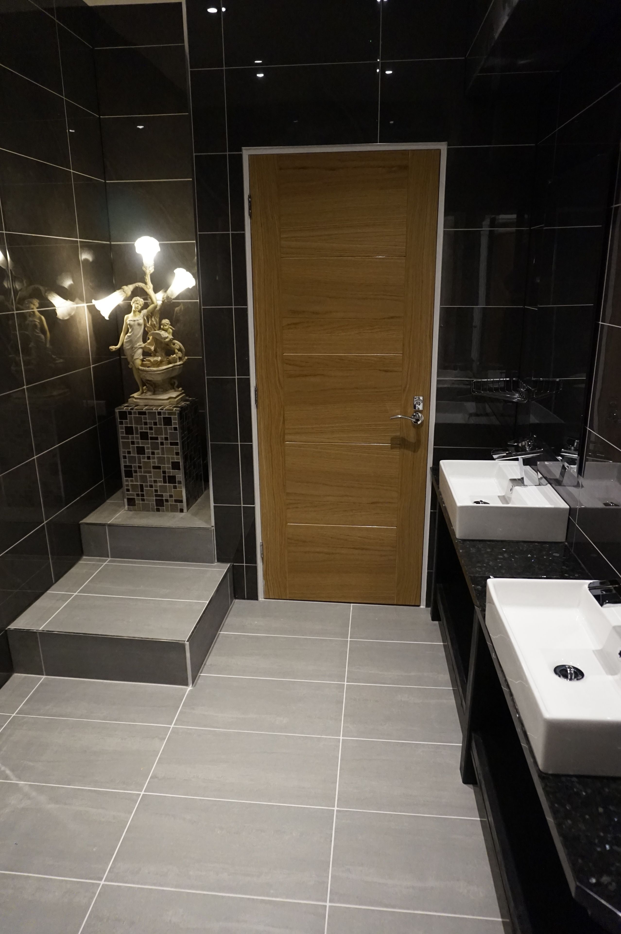 A modern bathroom with a wooden door, two sinks, and a mosaic tile wall.