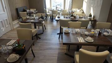 Comedor con varias mesas dispuestas para el servicio, sillas y vistas de la ciudad a través de amplias ventanas.