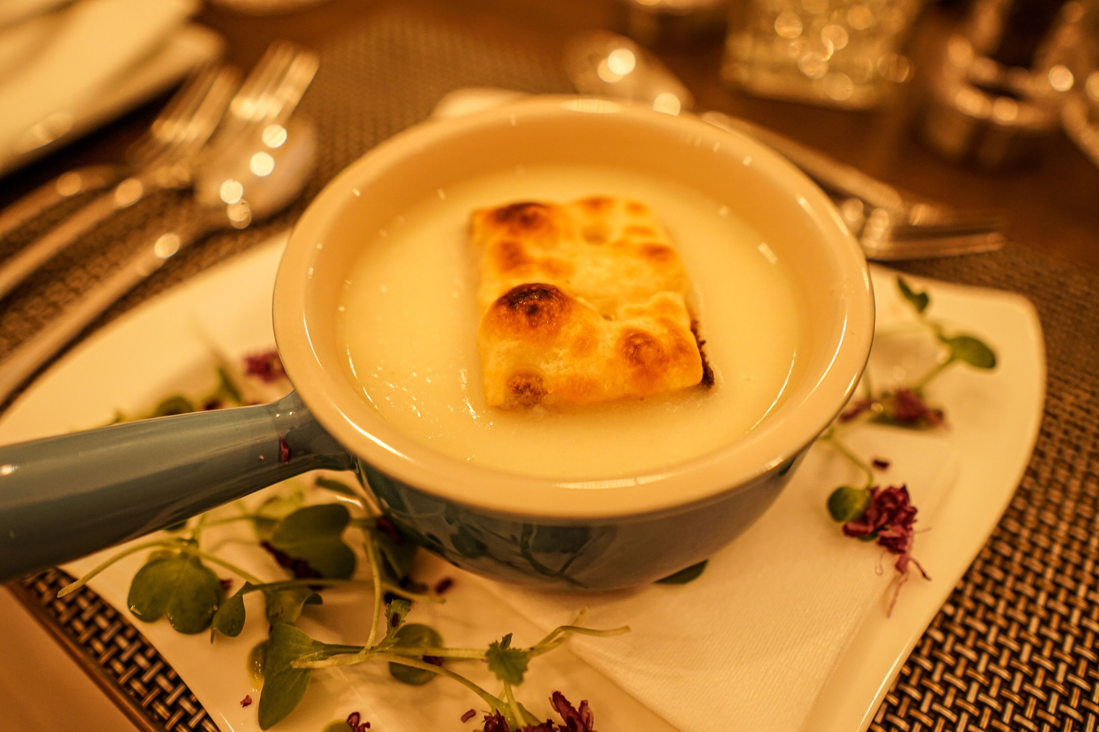 A bowl of soup with a piece of bread on the side, placed on a white plate with a floral napkin underneath.