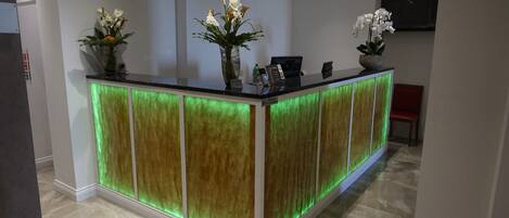 A reception desk with a modern design, featuring a green illuminated panel and two vases with flowers.