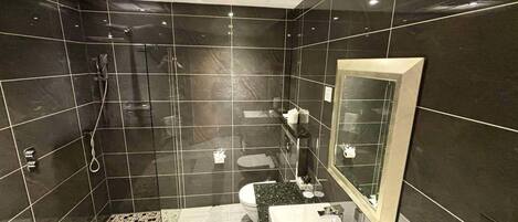 Un baño moderno con baldosas oscuras, una cabina de ducha de vidrio, un lavamanos con espejo y un suelo estampado.