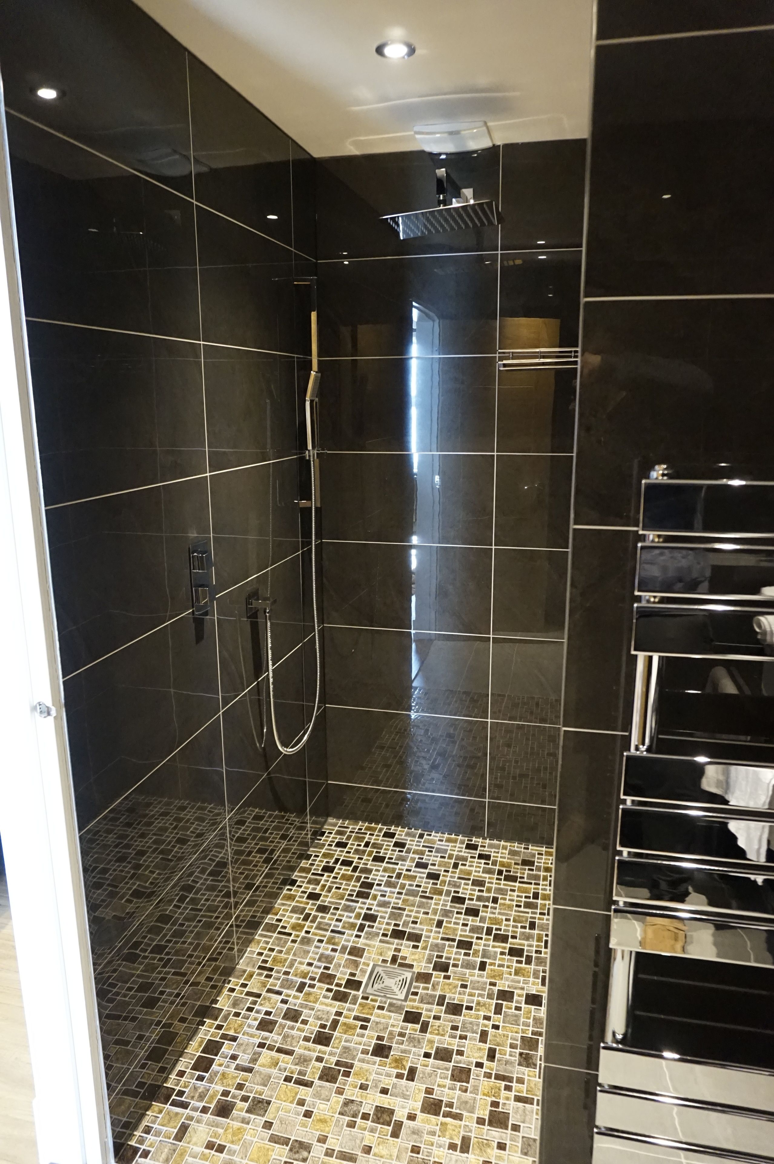 Un baño moderno con azulejos negros, ducha y suelo de mosaico.