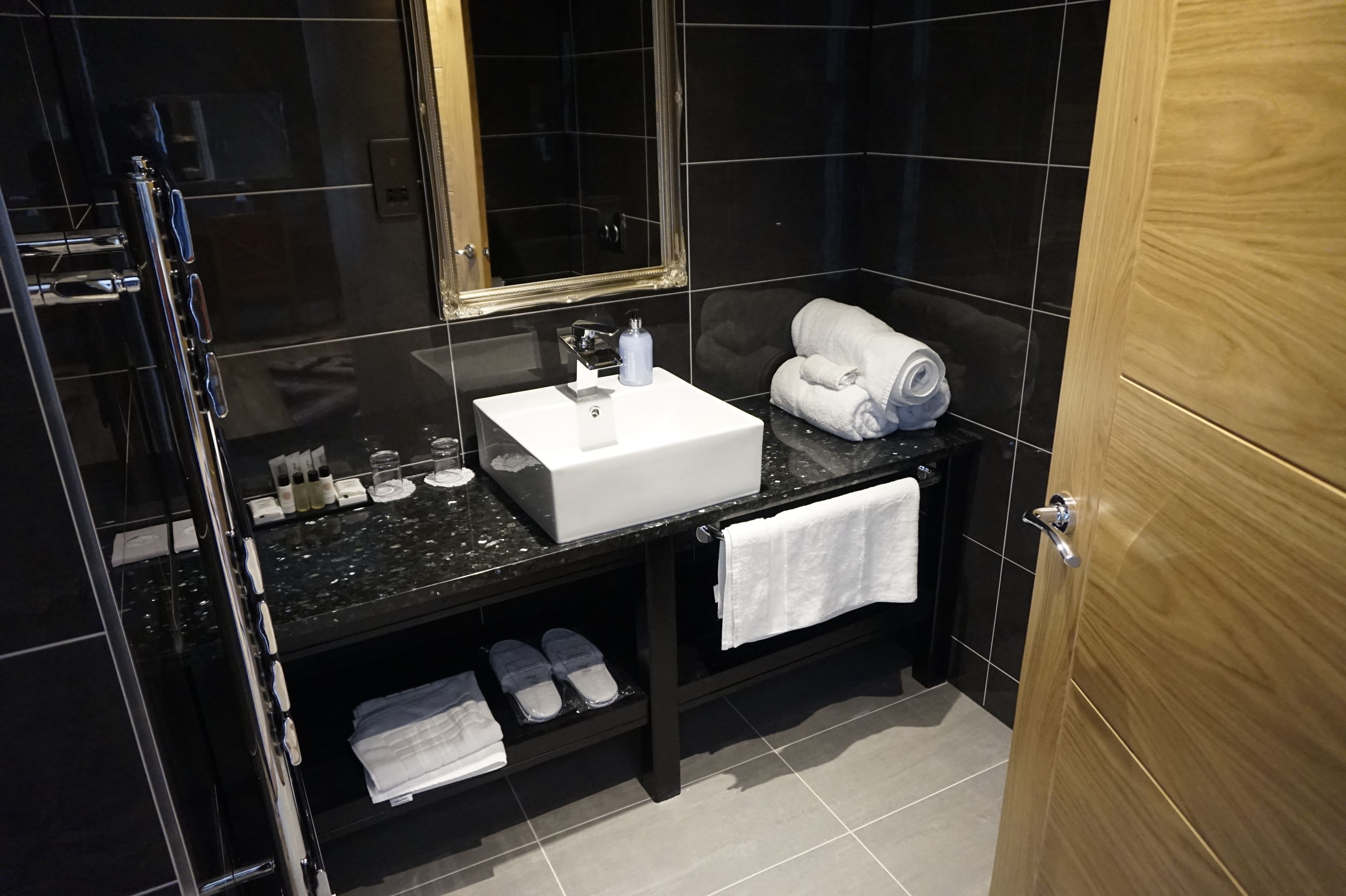 A modern bathroom with a black marble countertop, a white sink, a mirror, and a wooden door.
