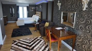A modern bedroom with a large bed, a sofa, a dining table, and a mirror.
