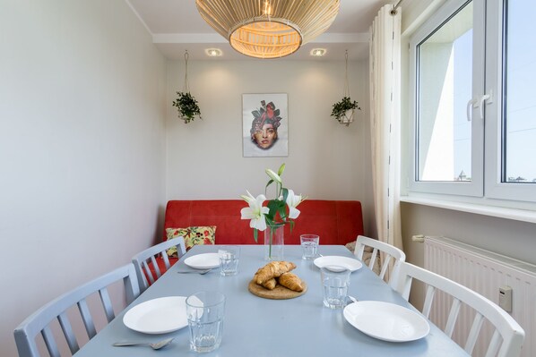 Un comedor con una mesa dispuesta para dos personas, un banco rojo y una ventana con persianas.