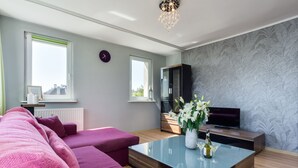 A modern living room with a sofa set, a glass coffee table, a TV, and a decorative vase. - Elite Apartments Sopot City Center (Sopot)