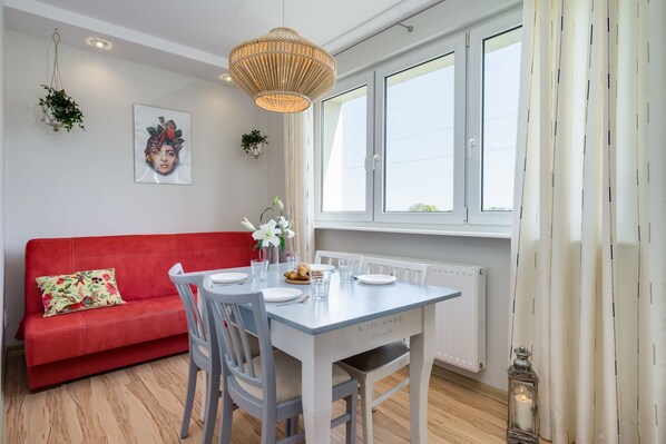 Un comedor con una mesa blanca, sillas grises, un sofá rojo y una planta colgante.