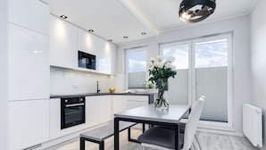 Una cocina moderna con gabinetes blancos, un horno negro y una zona de comedor con mesa y sillas.