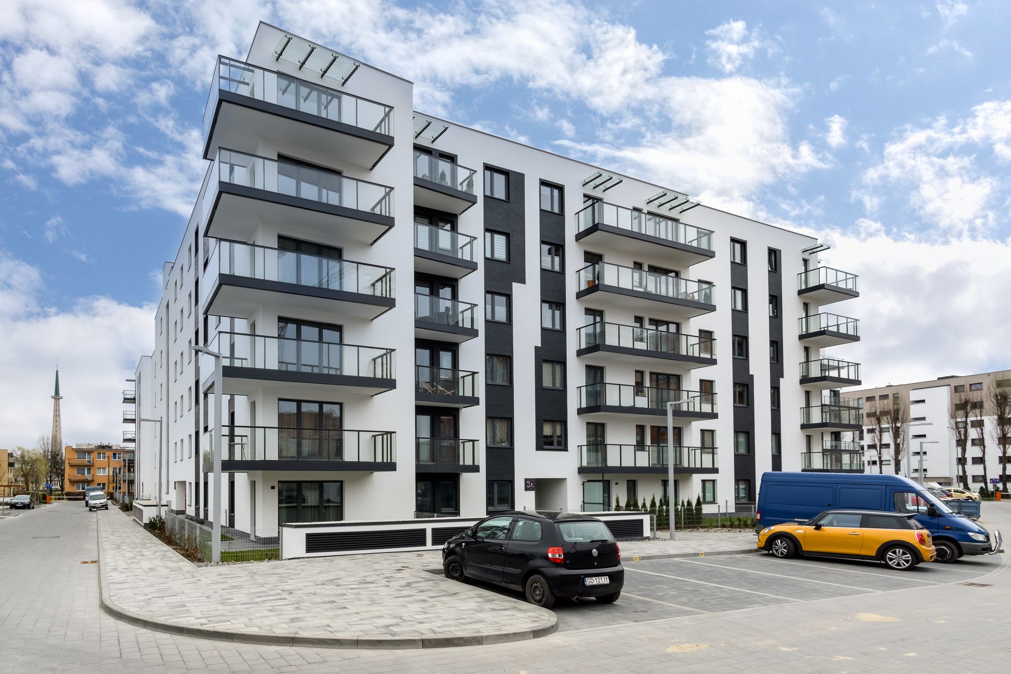 Un immeuble résidentiel moderne à plusieurs étages, doté de balcons, d’un espace de stationnement et offrant une vue sur un ciel dégagé.