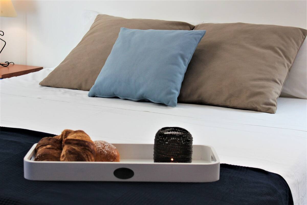 A bed with two pillows, a tray with croissants and a decorative item.