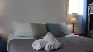 Un lit bien fait, avec une couette grise, des oreillers blancs et turquoise, et deux serviettes blanches roulées.