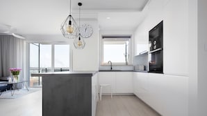 A modern kitchen with white cabinetry, a central island, and pendant lighting. - Elite Apartments Cityview Center (Gdansk)