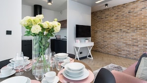 A modern dining area with a round table set for four, a vase of white flowers, and a kitchen in the background. - Elite Apartments Cityview Center (Gdansk)