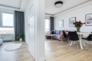 A modern living room with a sofa, dining table, and chairs, a potted plant, and a view of the city through large windows. - Elite Apartments Cityview Center (Gdansk)