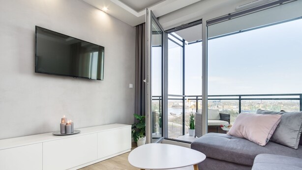 A modern living room with a flat-screen TV, a round table, a grey sofa, and a balcony with a view. - Elite Apartments Cityview Center (Gdansk)