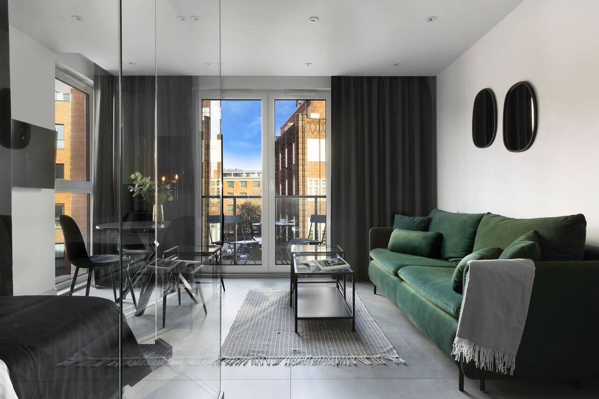 A modern living room with a green sofa, a glass dining table, and a view of the city through large windows.