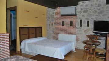 A bedroom with a bed, a TV, a brick wall, and a wooden chair.