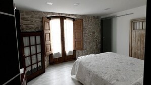 Un dormitorio con cama, pared de piedra, puerta de madera y ventana con cortinas.