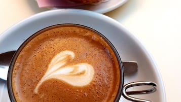 A cup of coffee with a heart design on the foam, a plate with a piece of pie, and a spoon on a napkin.