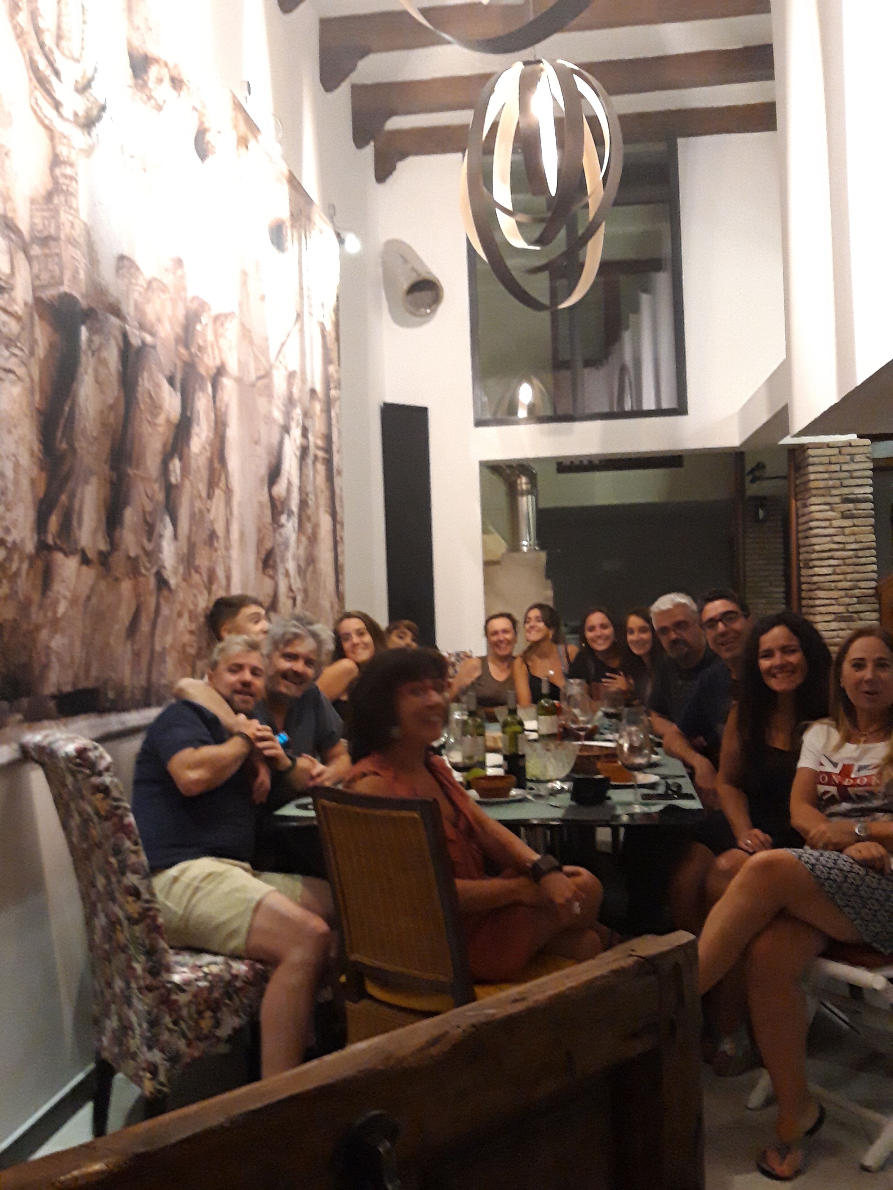 Un grupo de personas sentadas alrededor de una mesa en un comedor con decoración rústica, incluyendo una pared de piedra y una lámpara colgante.