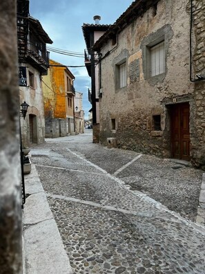 A narrow cobblestone street flanked by old stone buildings with visible doorways and windows. - Hospederia Jaramillo (Penaranda de Duero)